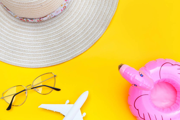 Summer beach composition. Minimal simple flat lay with plane sunglasses hat and Inflatable flamingo isolated on yellow background. Vacation travel adventure trip concept. Top view copy space. - Photo, Image