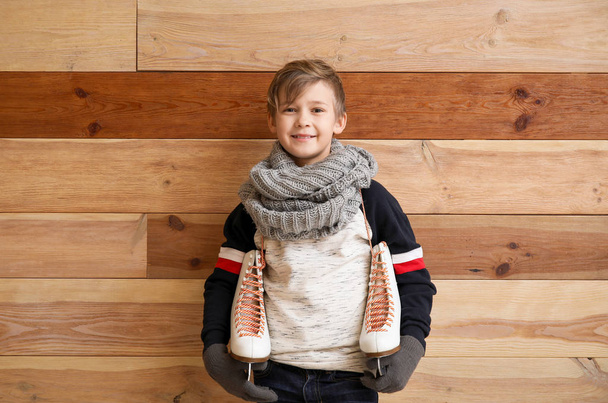 Cute little boy with ice skates against wooden background - Foto, afbeelding
