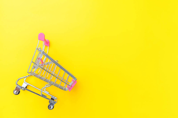 kleiner Supermarkt-Einkaufswagen zum Einkaufen Spielzeug mit Rädern isoliert auf gelben bunten trendigen modernen Modehintergrund. Verkauf kaufen Einkaufszentrum Marktladen Verbraucherkonzept. Kopierraum. - Foto, Bild