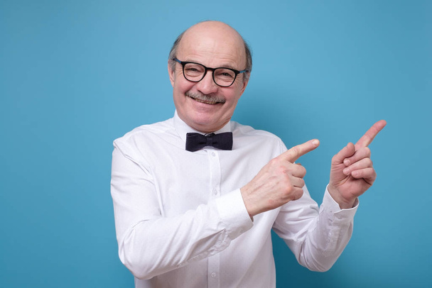 senior man with satisfied expression, indicates with fore fingers aside - Fotoğraf, Görsel