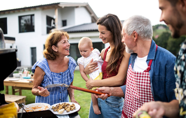 Portrait of multigeneration family outdoors on garden barbecue, grilling. - Фото, изображение