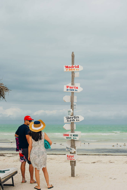 Isla Holbox, Μεξικό - Φεβρουάριος 2020 Νέοι ταξιδιώτες στην παραλία με μια πινακίδα που δείχνει τις κοντινές πόλεις και το τοπικό φαγητό. - Φωτογραφία, εικόνα