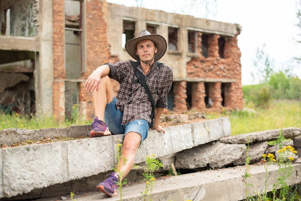 Un homme avec un chapeau de cow-boy est assis au milieu d'une maison en ruine
. - Photo, image