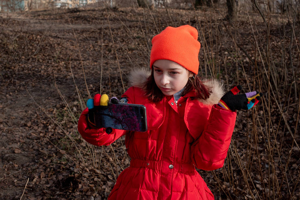 Sevimli kız, kırmızı ceketli, fotoğraf çekmek için poz veriyor ya da akıllı telefonuyla kendi fotoğrafını çekiyor. - Fotoğraf, Görsel