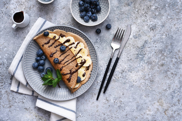 Crepe with banana, chocolate sauce and blueberries for breakfast on a stone background. - Foto, Imagen