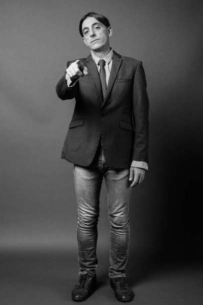 Studio shot of mature handsome Italian businessman against gray background in black and white - Fotoğraf, Görsel