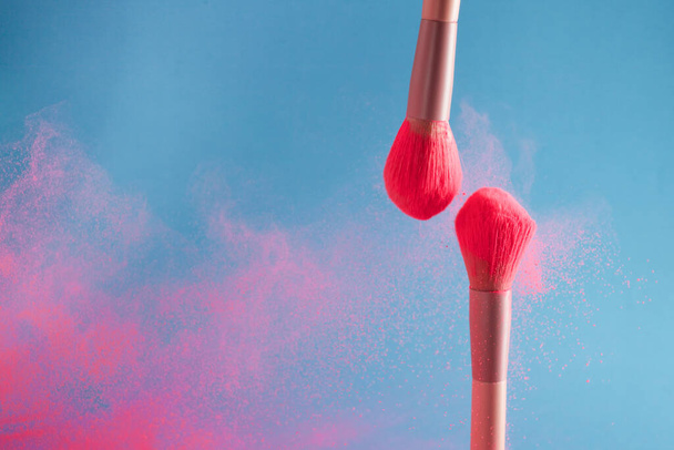 close-up photo of two professional make-up brushes with pink powder in motion on blue background - Фото, зображення