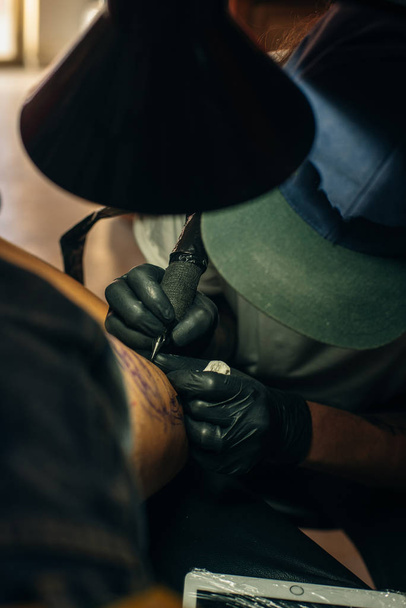 Gros plan de tatoueur professionnel faisant photo sur place de l'homme à la machine encre noire d'un bocal
.  - Photo, image