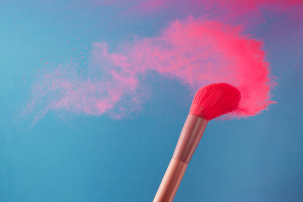 close-up photo of two professional make-up brushes with pink powder in motion on blue background - Фото, изображение