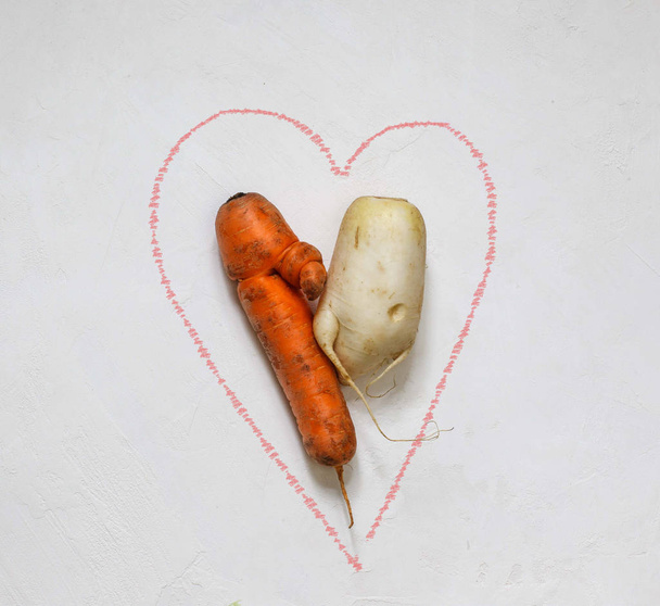 Потворна морква і редька дакону в центрі рожевого серця намальованого на білому тлі
 - Фото, зображення