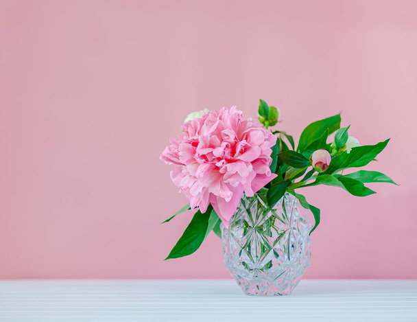 Pink peonies in a crystal vase on a pink wood background. - Foto, Bild