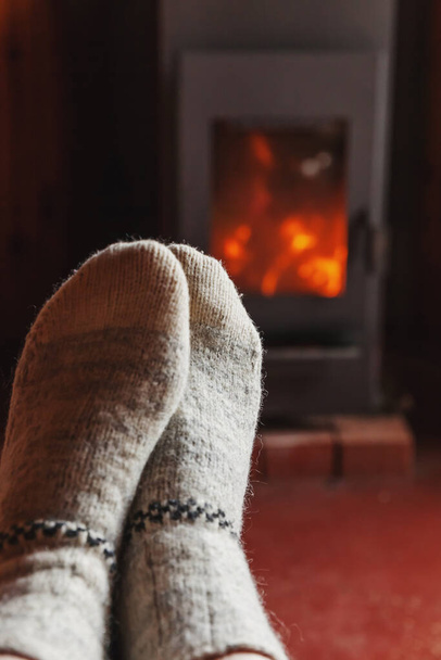 暖炉の背景に冬服のウールの靴下の足。冬や秋の夜に家に座ってリラックスして暖まる女性。冬と寒さの概念。巨大なクリスマスの前夜. - 写真・画像