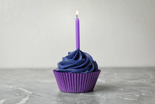 Смачний кекс на день народження з вершками та палаючою свічкою на мармуровому столі
 - Фото, зображення