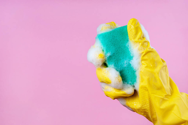 Gloved hand holds a foam sponge on a pink background copy space - Photo, Image