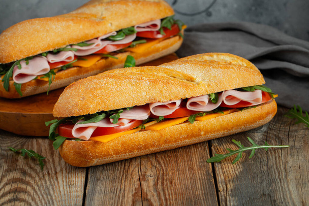 アルグラと2つの長いバゲットサンドイッチ,新鮮なトマトのスライス,ハムとチーズ. - 写真・画像