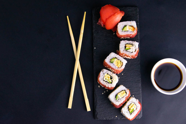 Des rouleaux sur un support de granit pour les sushis sont disposés sous la forme d'un dragon, à côté de bâtons debout pour les sushis et la sauce soja
. - Photo, image