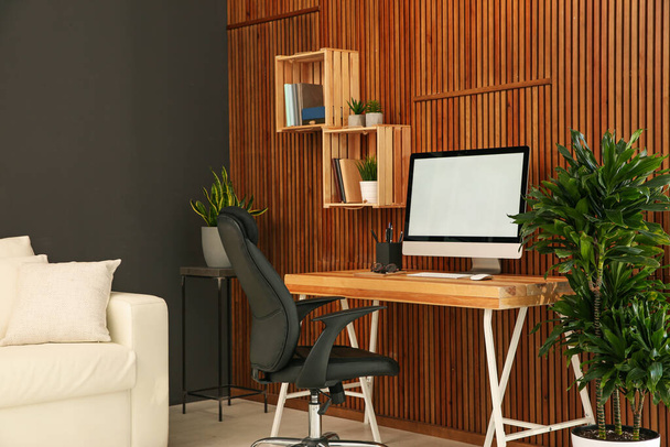 Comfortable workplace with computer near wooden wall in stylish room interior. Home office design - Foto, immagini