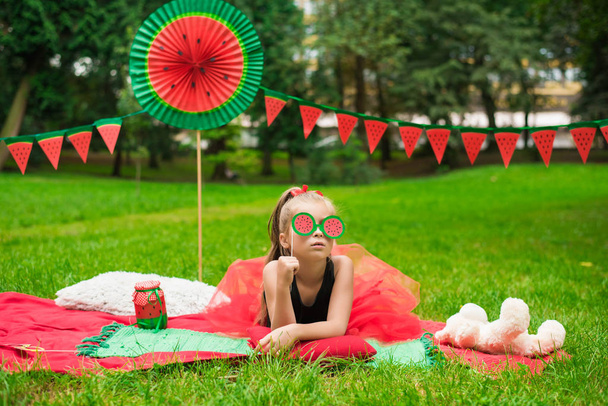 Impreza arbuzowa, piknik dla dzieci w parku. Dzień arbuza. Cute mała dziewczynka z okularami. - Zdjęcie, obraz