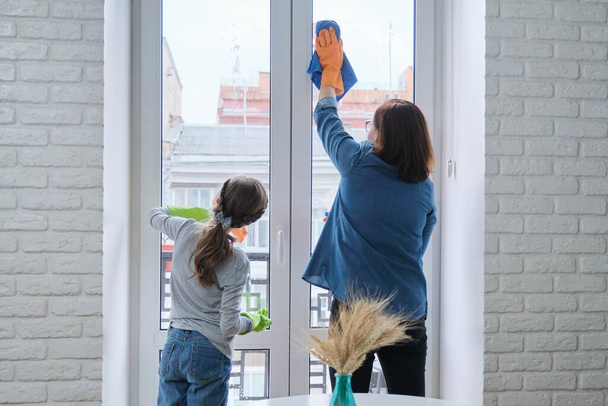 Mother and daughter child in gloves with detergent rag cleaning windows together - Foto, Imagen