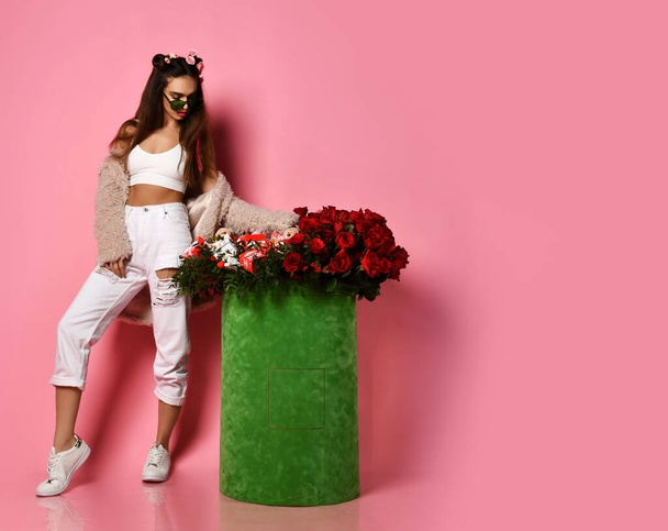 Young beautiful happy brunette woman in stylish casual clothing and sneakers standing near huge valentines day box of flowers - Foto, Imagem