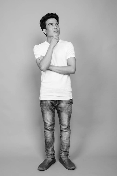 Estudio de hombre joven asiático sobre fondo gris en blanco y negro - Foto, Imagen