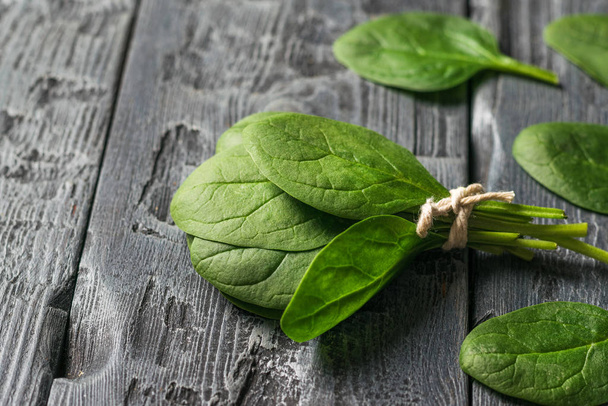 Tied in a bunch of spinach leaves on a black wooden table. Food for fitness. - Photo, Image