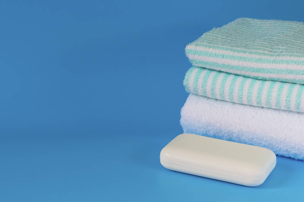 Zachte en donzige handdoeken op een blauwe achtergrond. Zeep voor bad, wasserij en lichaamsverzorging. Persoonlijke hygiëne producten. Badkameraccessoires. - Foto, afbeelding