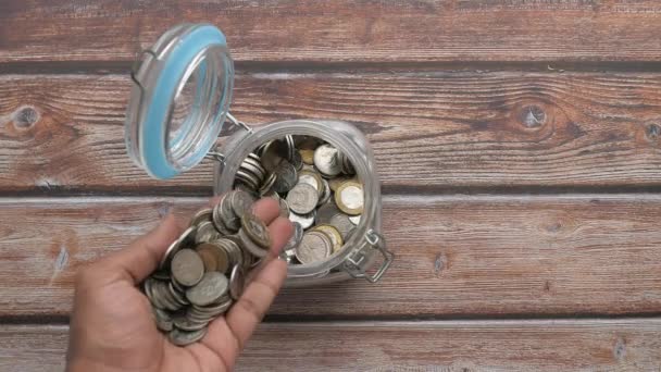 top widok człowiek ręka oszczędności monety w słoiku  - Materiał filmowy, wideo