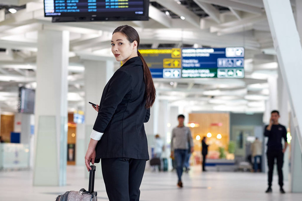 asian business woman at the airport with trolley bag, near the flight display looking flight schedule - Foto, imagen