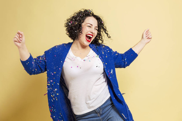 Dancing and laughing beautiful young woman plus size in jeans and a blue sweater. Yellow background. - Photo, image
