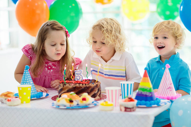子供の誕生日パーティー。ケーキのろうそくを吹いている子 - 写真・画像