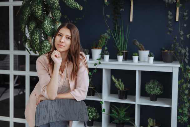 A brunette in a cream sweater is looking at the screen. In the background are growing diverse houseplants - Foto, Imagem