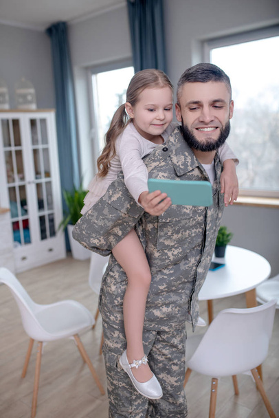 Young man in uniform holding a little girl on his back. - Foto, afbeelding