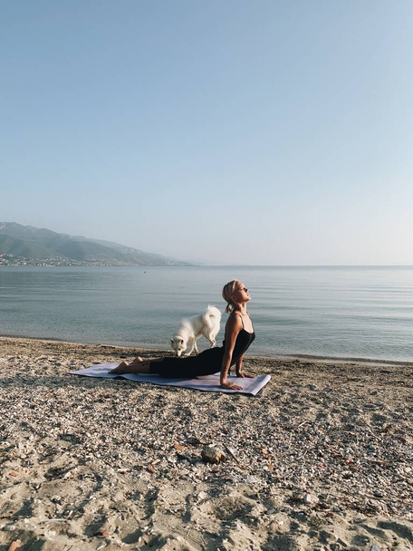 Mladá blondýnka dívka surya namaskar jóga asana na mořském břehu při východu slunce - Fotografie, Obrázek