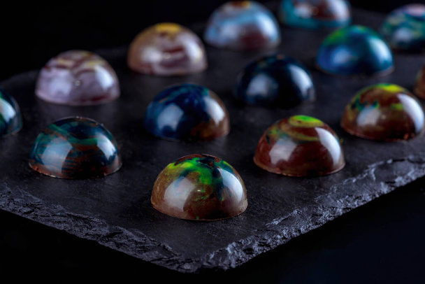Gastronomic ideas. Handmade chocolate candies in colored glaze. Black background. Close-up. - Foto, Imagen