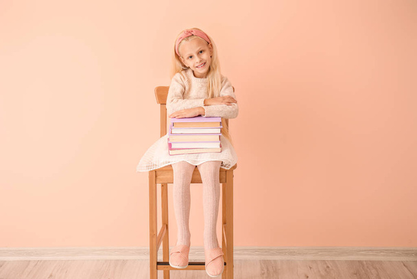 Kislány könyvek ül a széken közel színes fal - Fotó, kép
