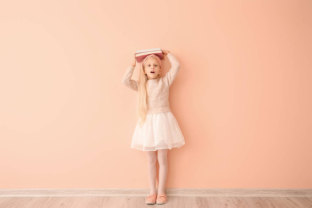 Surprised little girl with books near color wall - Photo, Image