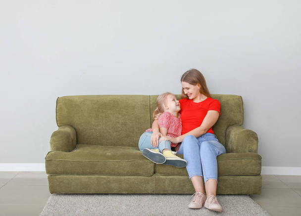 Onnellinen nuori äiti ja tytär istuu sohvalla lähellä valoseinää
 - Valokuva, kuva