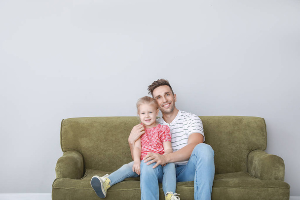 Szczęśliwy młody ojciec i córka siedzi na kanapie w pobliżu światła ściany - Zdjęcie, obraz