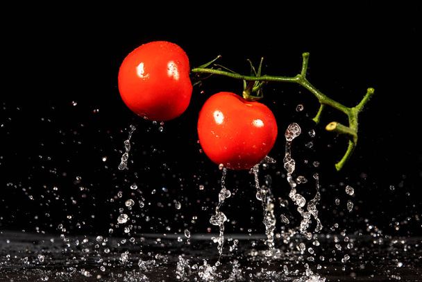 Помідор у воді. Вода розбризкує свіжі червоні помідори на чорному тлі
 - Фото, зображення