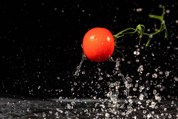 Помідор у воді. Вода розбризкує свіжі червоні помідори на чорному тлі
 - Фото, зображення