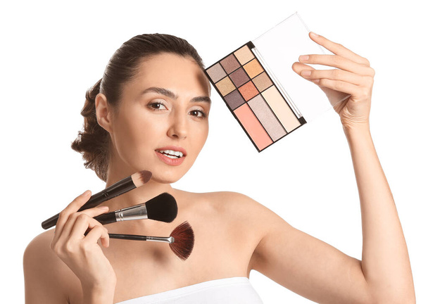 Beautiful young woman applying makeup on white background - Photo, Image