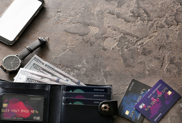 Portemonnee met creditcards, geld, mobiele telefoon en klok op grunge achtergrond - Foto, afbeelding