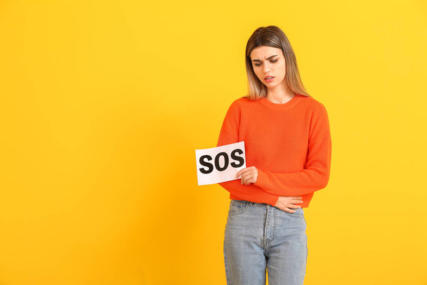 Jeune femme tenant du papier avec le texte SOS sur fond couleur. Concept de menstruation
 - Photo, image