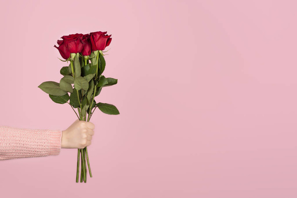 Bellissimo bouquet di rose rosse in una mano di donna su sfondo rosa chiaro
. - Foto, immagini