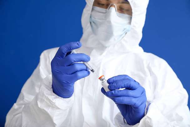 Laboratory worker in protective uniform and with vaccine on color background. Concept of epidemic - Foto, afbeelding