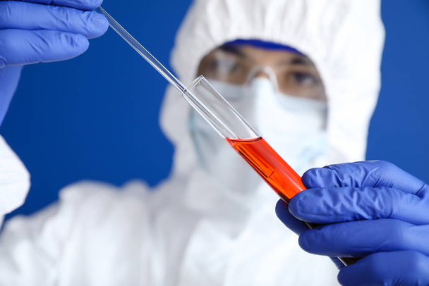 Laboratory worker in protective uniform and with sample in test tube on color background. Concept of epidemic - 写真・画像