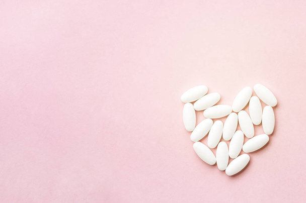 white heart from tablets and pills isolated on pink background with sunlight. - Fotó, kép