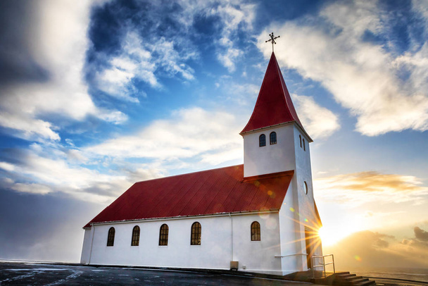 La pintoresca Iglesia Vik i Myrdal en Vik, Islandia. El sol se levanta sobre el mar detrás, causando llamaradas y una estrella del sol
. - Foto, imagen
