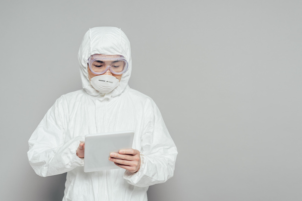 epidemiólogo asiático en traje de hazmat y máscara respiratoria usando tableta digital sobre fondo gris
 - Foto, imagen